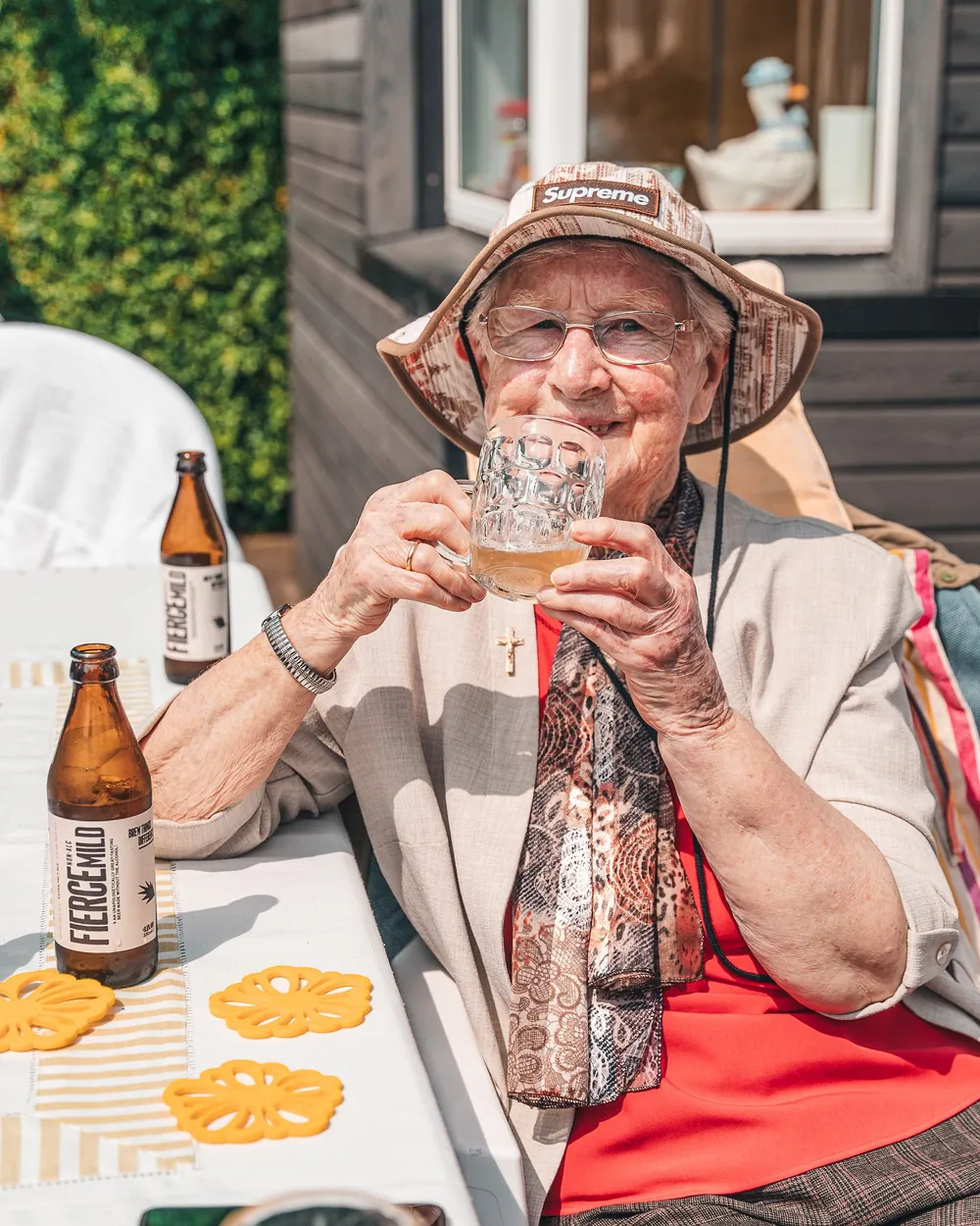 An older woman in a sun hat laughing over a glass of Fierce Mild at an outdoor table