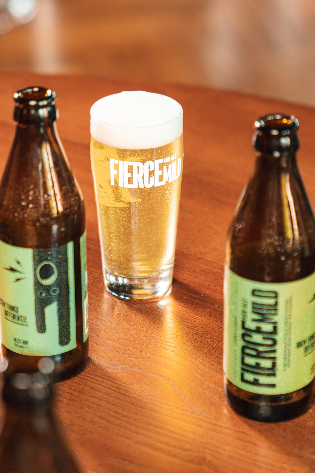 Two bottles of Fierce Mild Lively Lager and a full glass on a wooden pub table