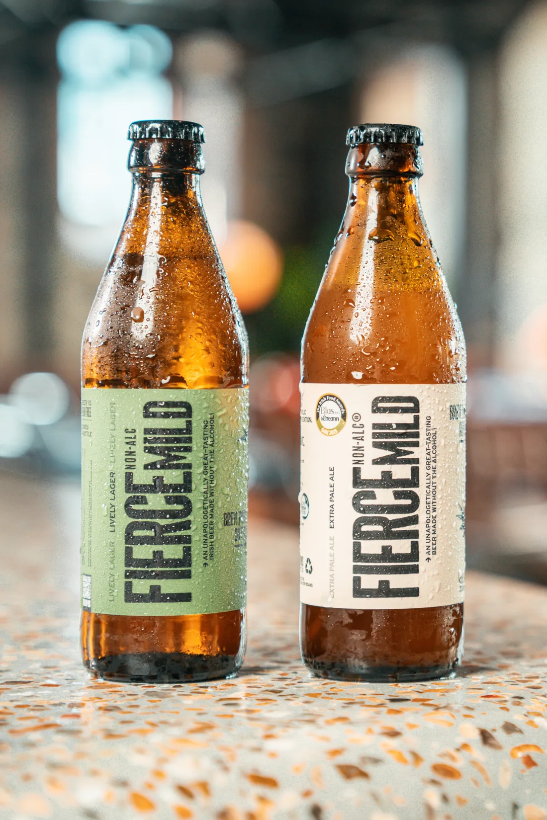 A bottle of Lively Lager and a bottle of Extra Pale Ale, beaded with condensation, on a terrazzo bar
