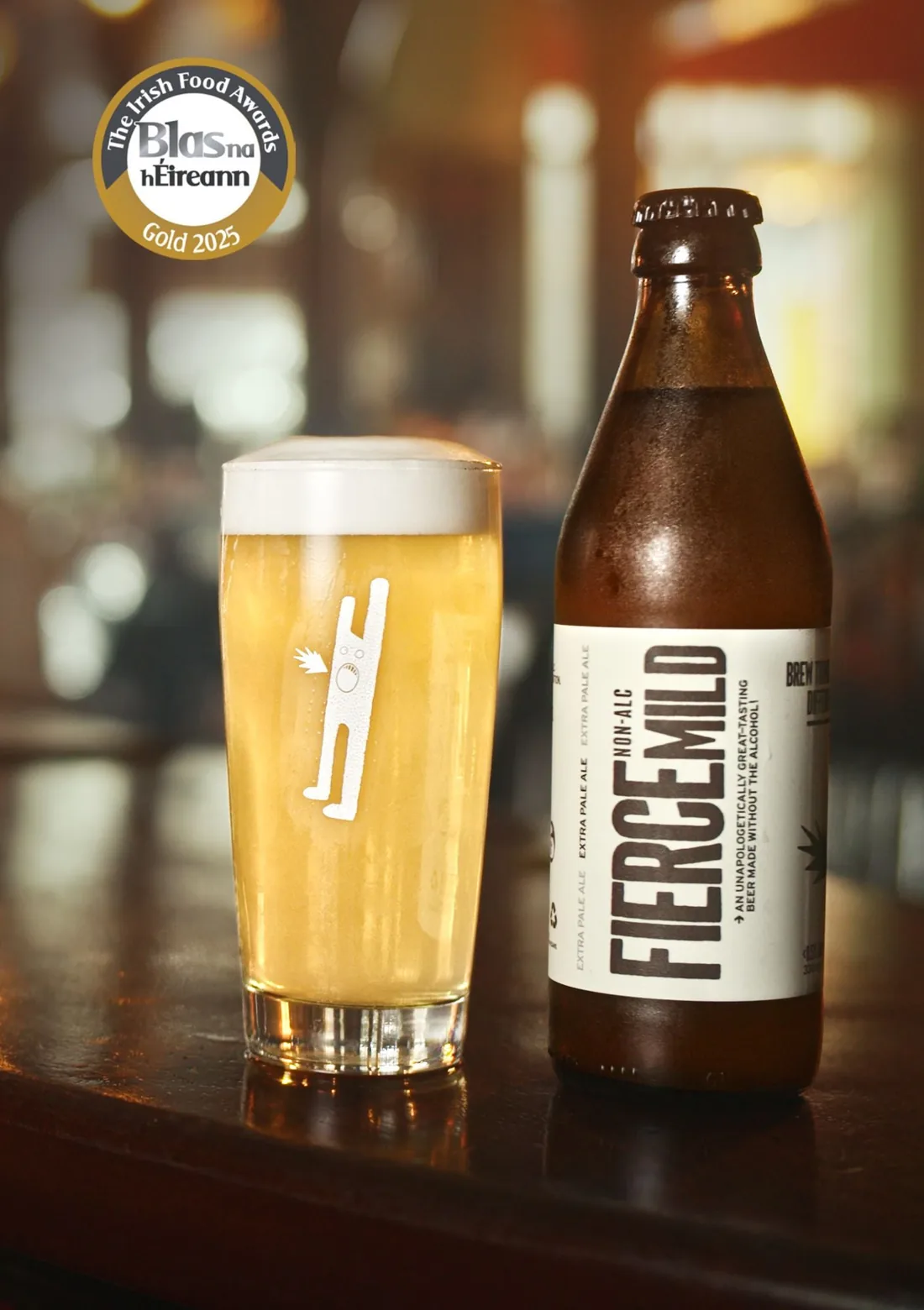 A pint of Fierce Mild Extra Pale Ale beside its bottle on a dark pub counter
